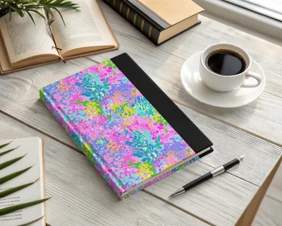 Journal with colorful abstract floral cover on a desk with coffee and a pen.