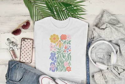 White t-shirt with a colorful floral graphic, laid flat with headphones and jeans.