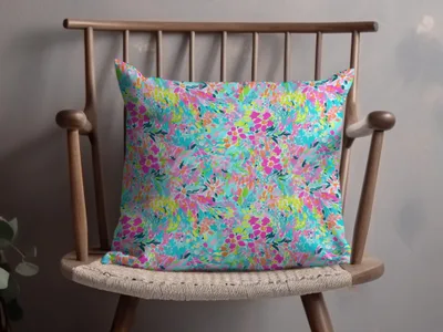 Floral print throw pillow in bright pinks, blues, and greens on a wooden chair.