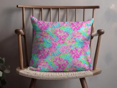 Bright floral pattern pillow with pink, blue, and green flowers on a wooden chair.