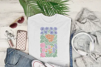White t-shirt with colorful floral illustration, surrounded by casual clothing and accessories.