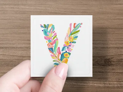 Hand holding a decorative letter V made of colorful floral elements.