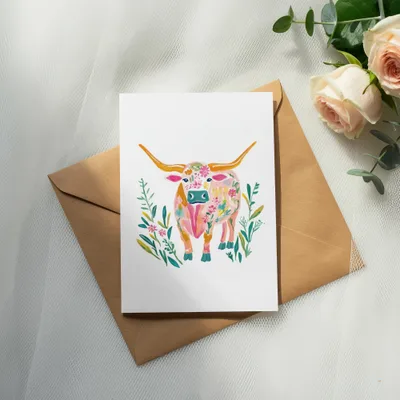 Watercolor painting of a longhorn cow with floral accents on a card.