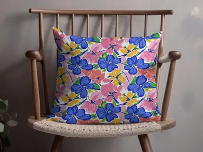 Floral throw pillow with blue, pink, and yellow flowers on a wooden chair.