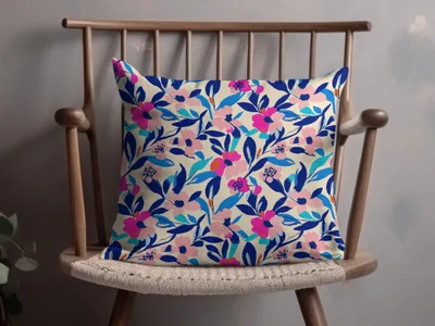 Cream pillow with vibrant pink and blue floral pattern on wooden chair.