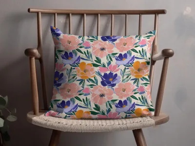 Throw pillow with a floral pattern in pink, purple, and orange on a wooden chair.