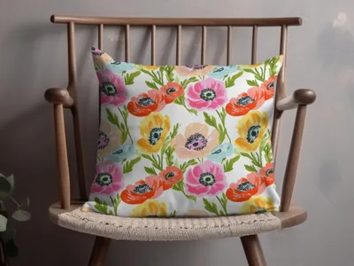 Floral pillow with pink, orange, and yellow poppies on a wooden chair.