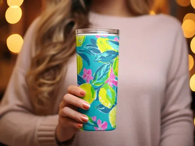 Tumbler with a vibrant lemon and floral print held by a woman.