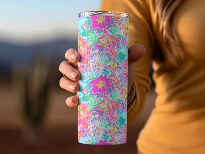 Person holding a skinny tumbler with a vibrant floral pattern of pink, blue, and green.