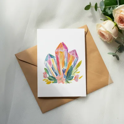 Watercolor illustration of colorful crystals and flowers on a card, resting on an envelope.