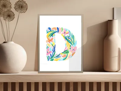 Colorful floral letter D print in a frame on a shelf.