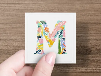 Floral patterned letter M on a white card held by a person.