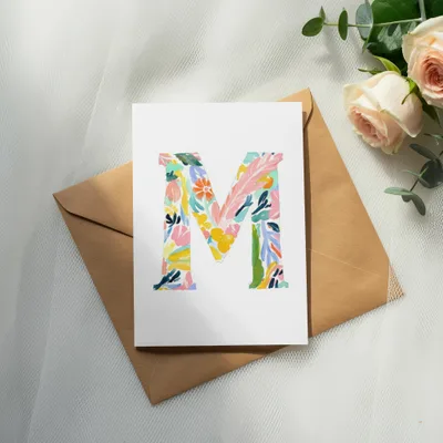 Watercolor floral initial 'M' on a card atop a brown envelope.