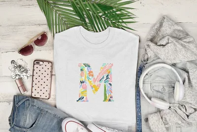 White t-shirt with colorful floral letter M graphic, styled with sunglasses, headphones, and jeans.