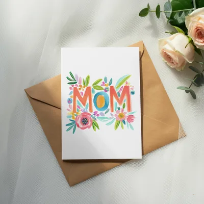 "MOM" in colorful floral lettering on a white card, atop a brown envelope.