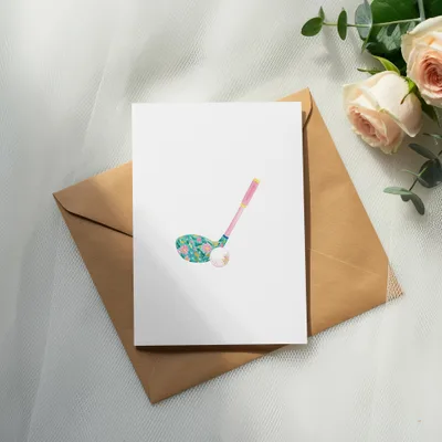 Golf club with floral pattern and golf ball on blank card, next to roses.