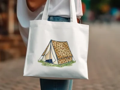 White tote bag with leopard print tent illustration on grassy field.