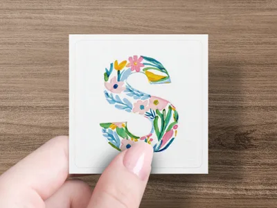 Hand holding watercolor letter S with floral pattern.