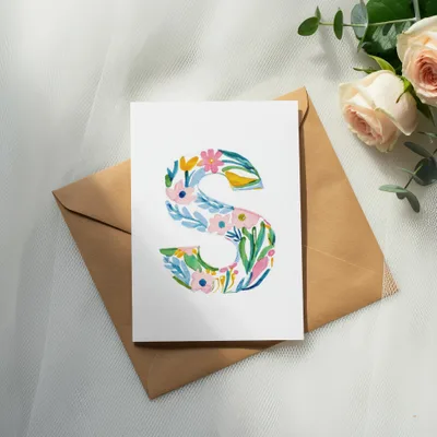 Watercolor floral letter "S" on a card with a brown envelope and roses.