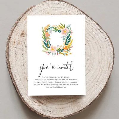Invitation card with floral wreath and "You're invited" text on wooden slice.