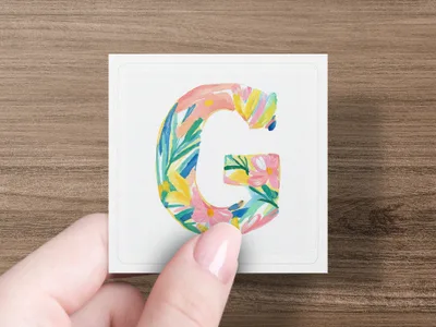 Floral letter G on card held by a hand.
