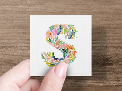 Floral letter S on a white card held by a hand.