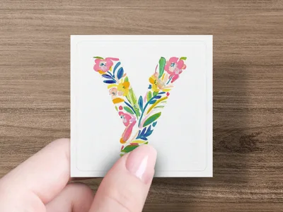 Hand holding a square card with a colorful floral letter "Y" design.