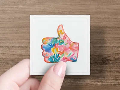 Colorful floral thumb up symbol on white card held by fingers.