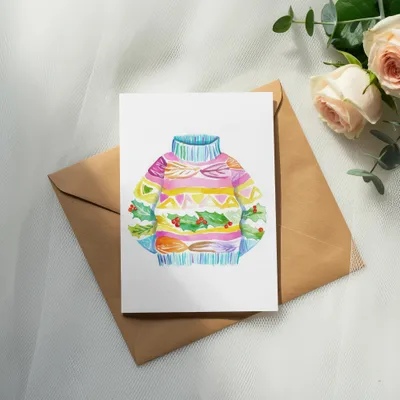 Watercolor illustration of a colorful holiday sweater with holly sprigs.