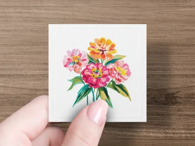 Hand holding a square card with a watercolor painting of pink and orange zinnias.