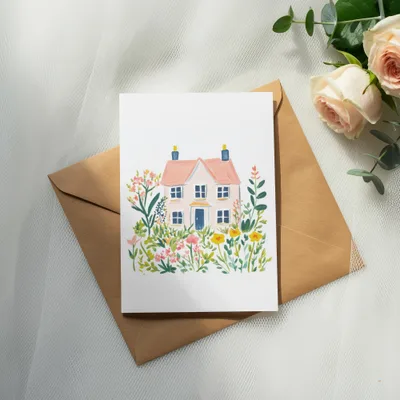 Watercolor illustration of a pink house surrounded by colorful flowers on a kraft envelope.